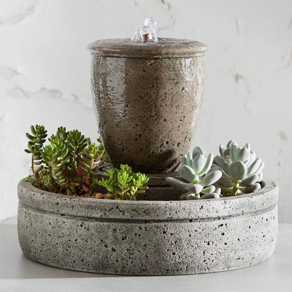 Cement indoor water feature surrounded by plants.