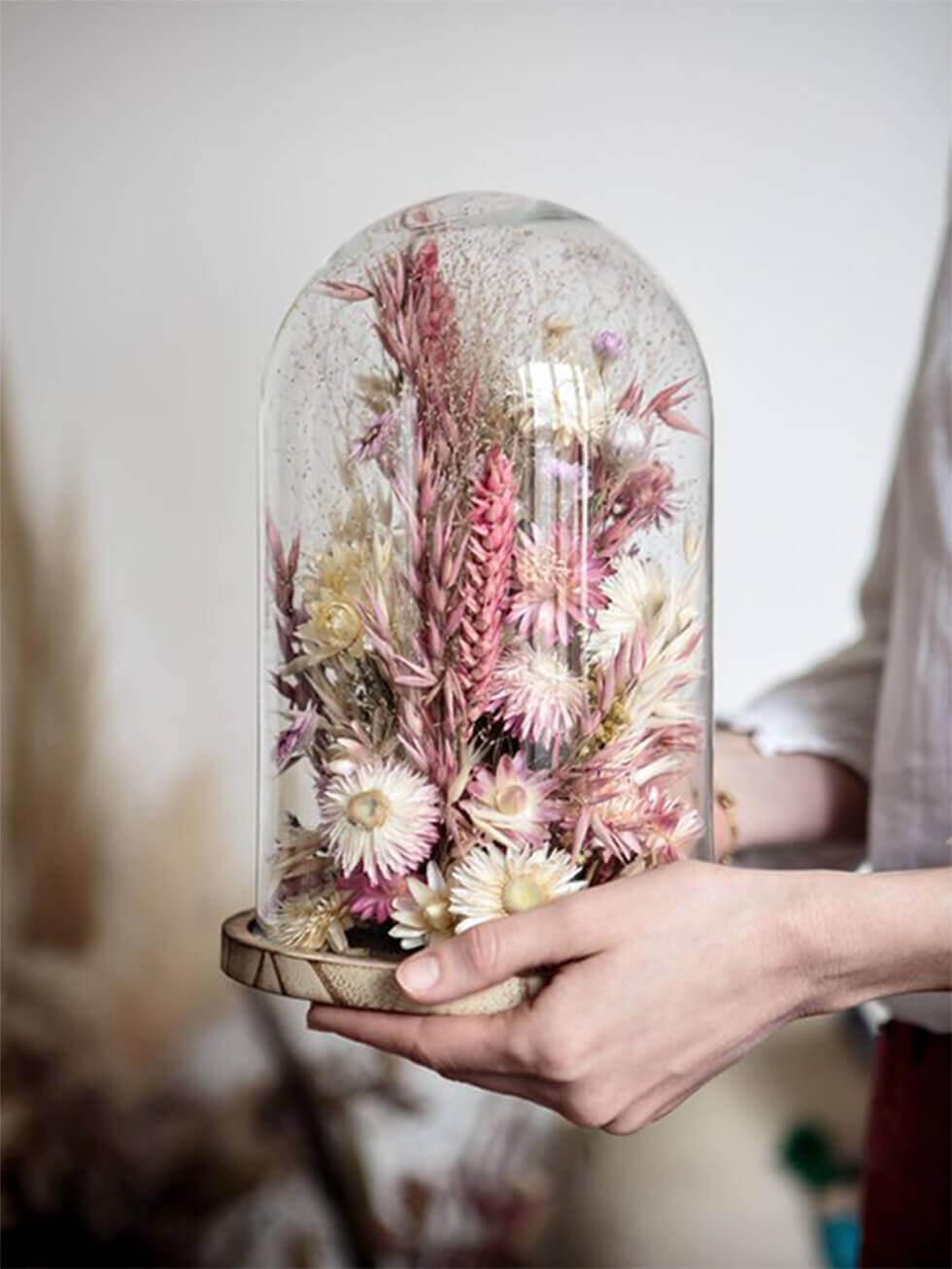 Dried flowers arranged in a sealed bell jar for decoration.