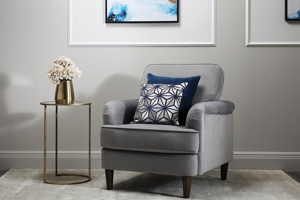Grey armchair beside a gold side table with thin legs.