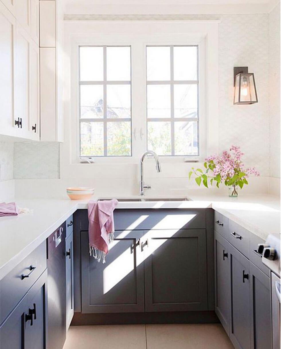 A well-lit, airy small kitchen with dark cupboards, white walls, and minimal, clean decor and natural light.