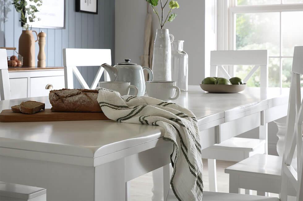 Close up of a white wooden extending dining table with matching chairs and blue walls