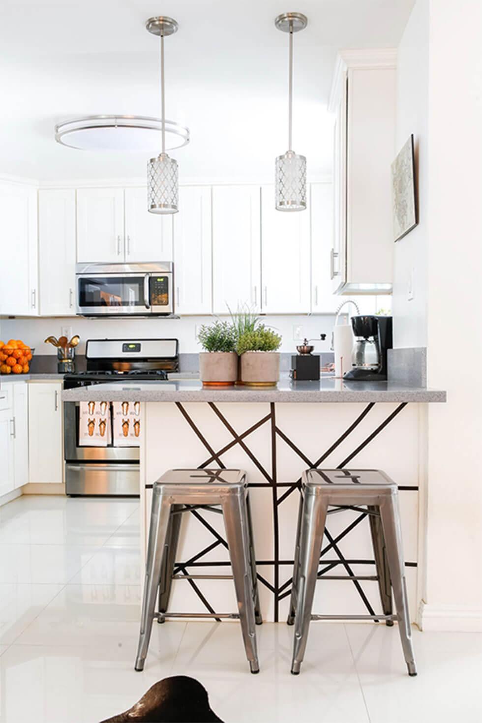 Simple small white kitchen with silver bar stools at a kitchen island with low lamps