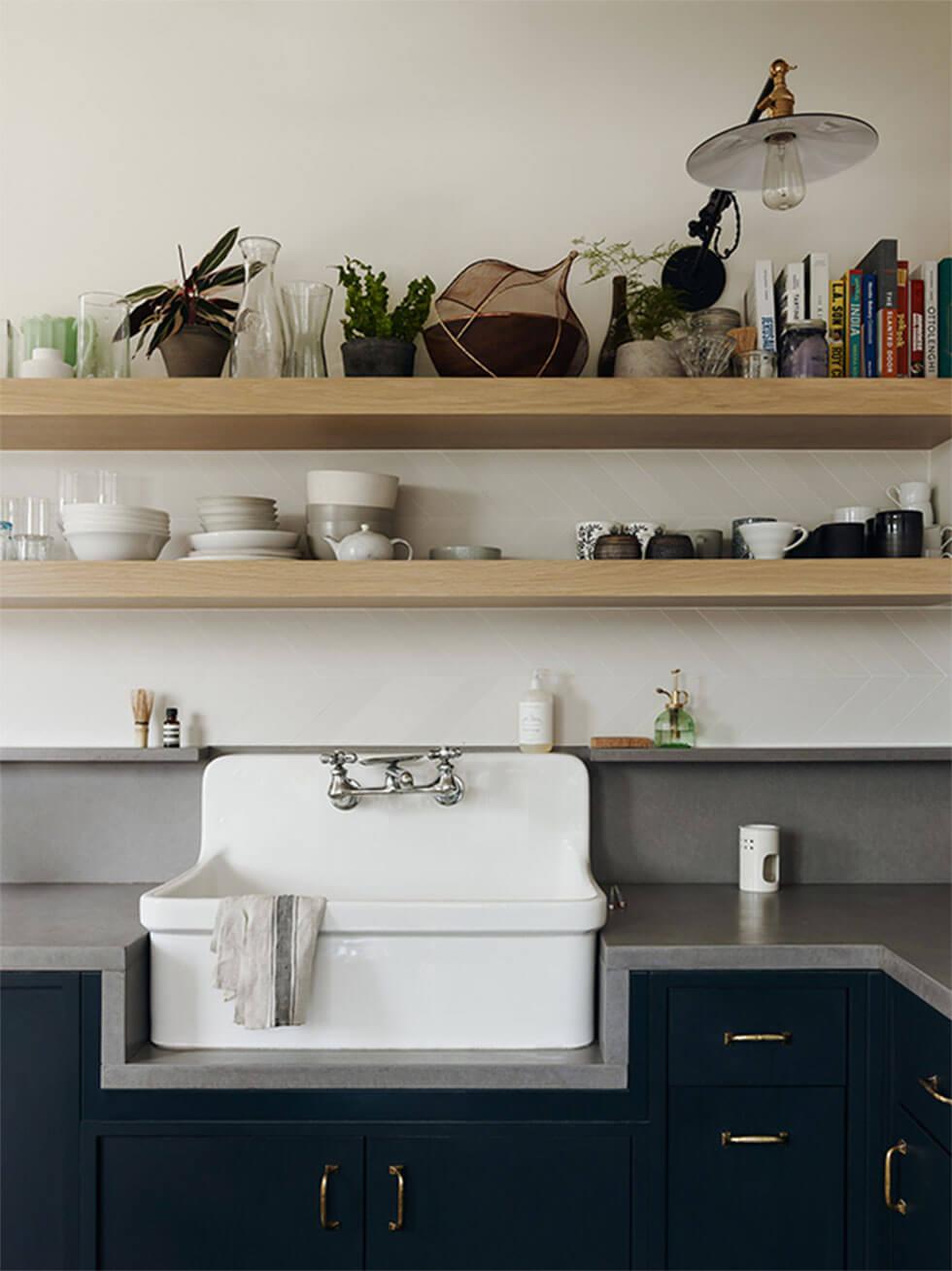 Minimal small kitchen with wooden shelves, white sink and dark grey counter tops and cabinets