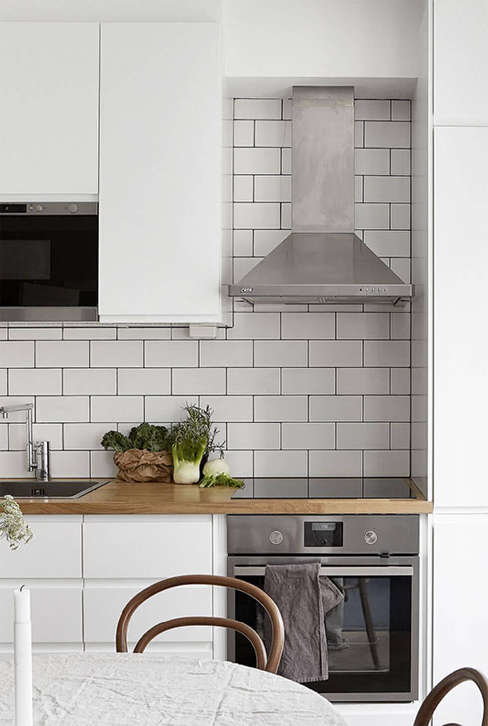 Small kitchen with white cabinets and dining table, subway tile backsplash and chrome cooking hood