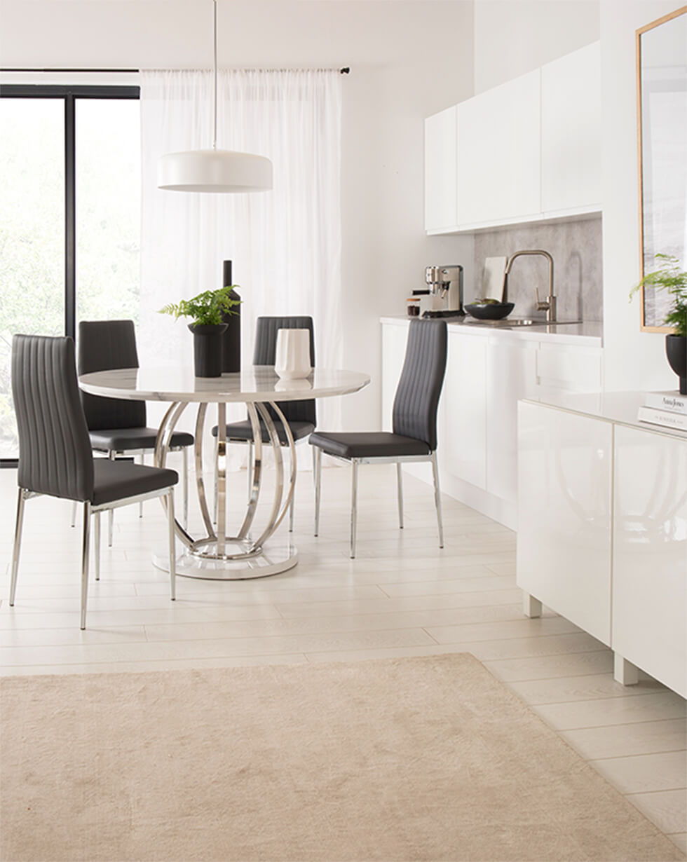 Round white marble dining table with chrome pedestal in minimalist dining room with black leather chairs