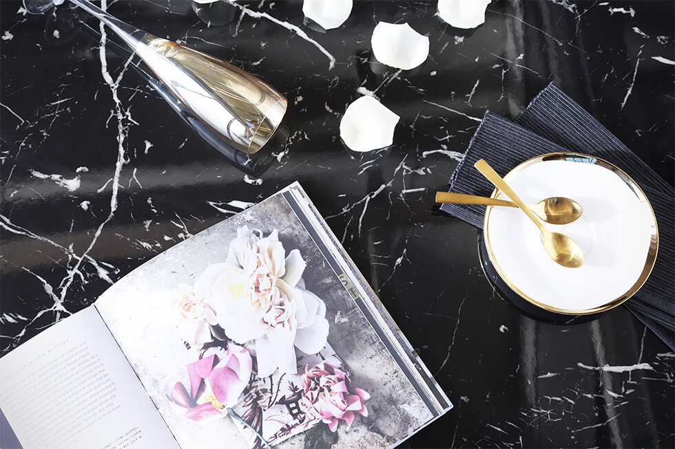 Flat lay of black marble dining table with gold tableware and coffee table book