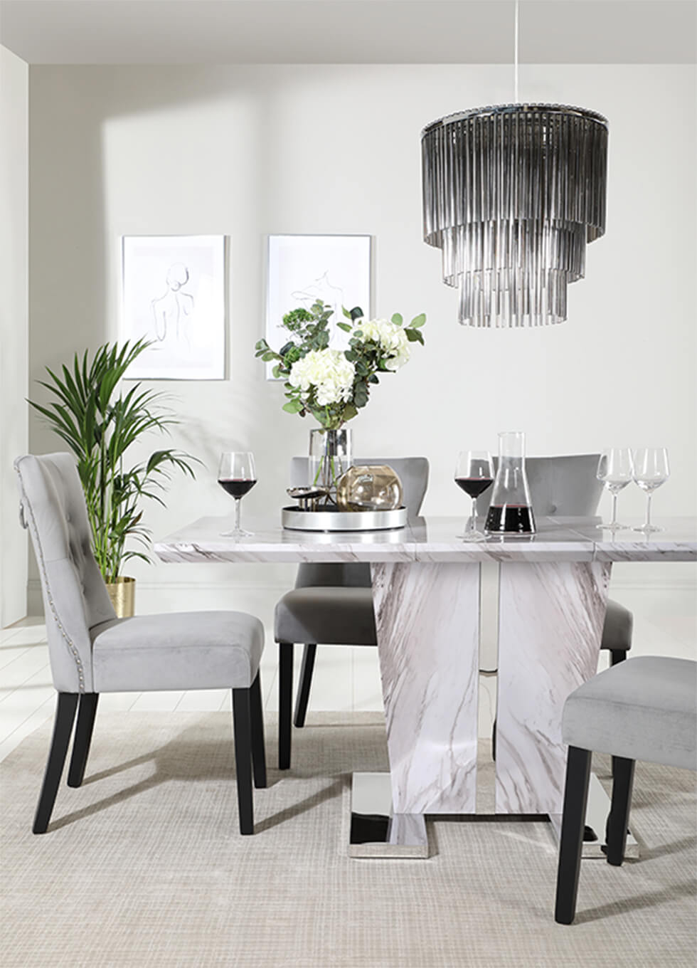 Neutral grey dining room with a grey marble dining table with a pedestal, fringe lamp and indoor plants