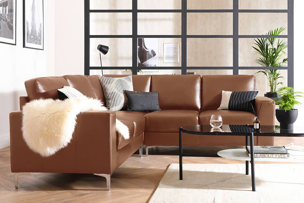 A brown leather corner sofa, crittall windows and black coffee table in an industrial style living room