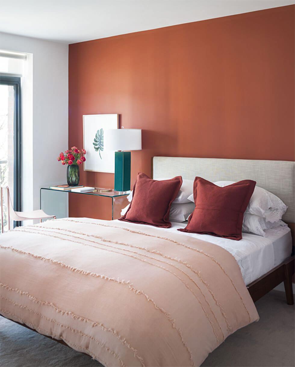 Bedroom with walls painted terracotta with a light neutral bed.