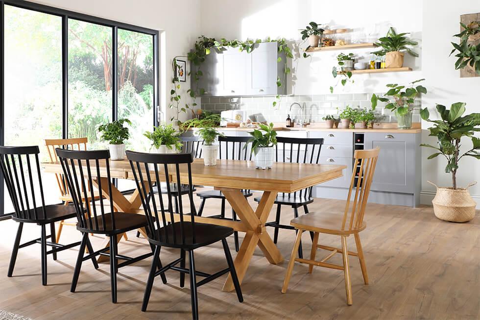 Large wooden dining table with mismatched black and wooden chairs with lots of plants