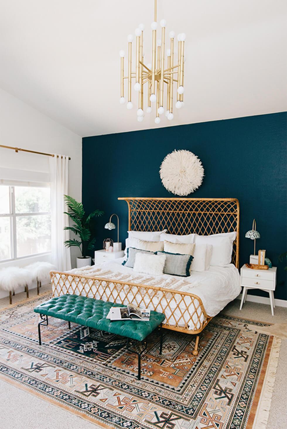 Tropical teal bedroom with a large rug, gold chandelier and statement rattan bed