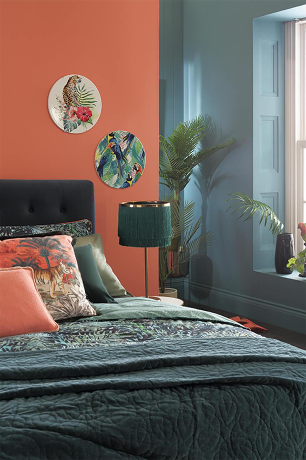 Tropical teal bedroom with contrasting orange and teal walls, and a dark velvet bed.