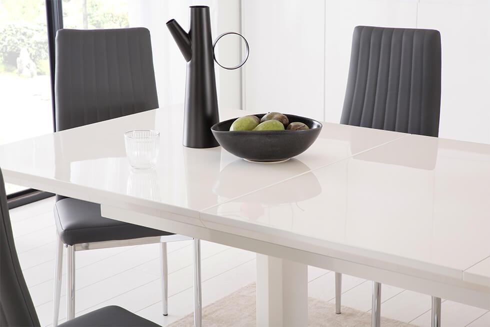 Close up of extending white high gloss dining table with black dining chairs