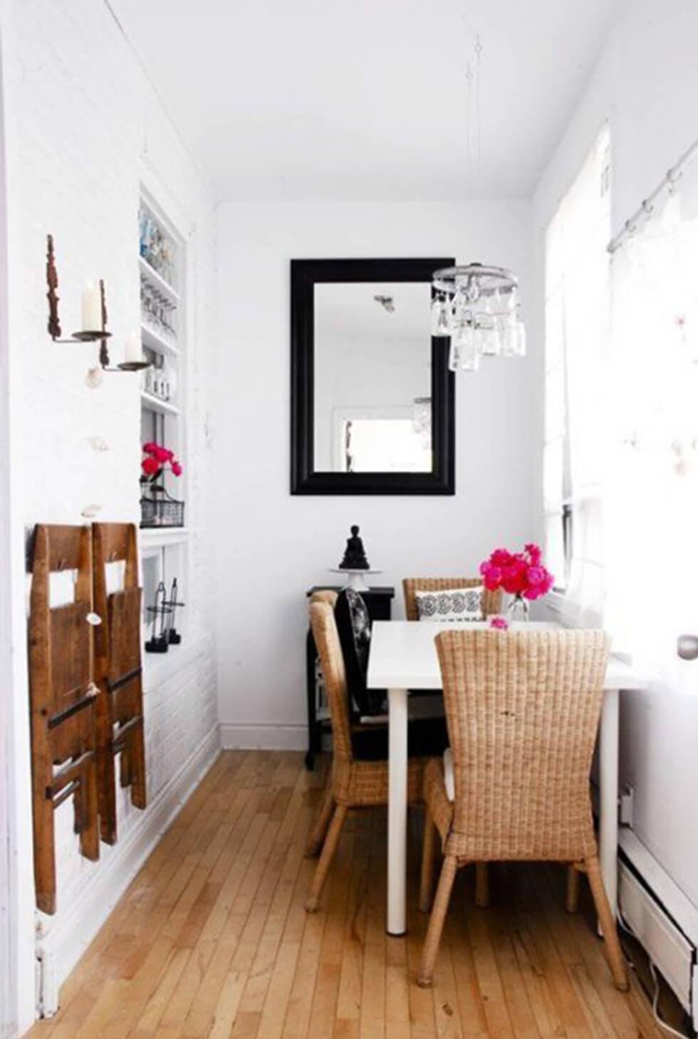 Bright and airy small dining room with white table against a wall, wicker chairs and a mirror