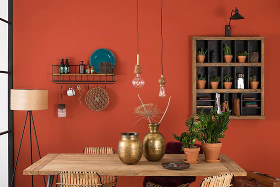 Small dining room with warm orange walls, wooden dining table, shelves and bronze decor