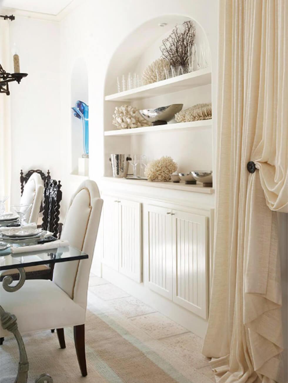 Arched alcove with shelves and cupboards in a neutral white dining room.