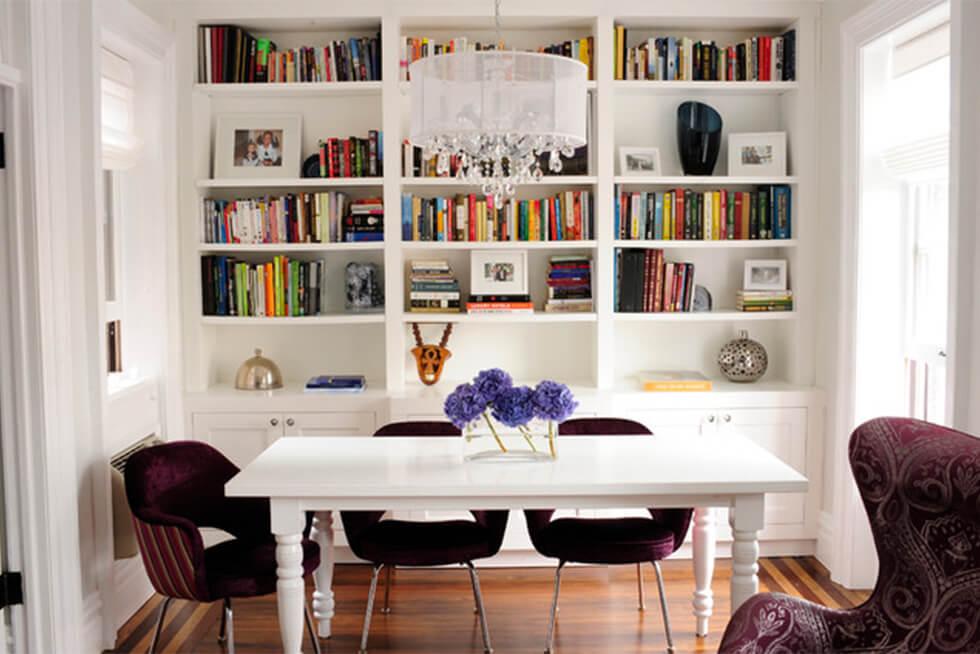 Modern dining room with dark velvet dining chairs, white table, and bookshelves