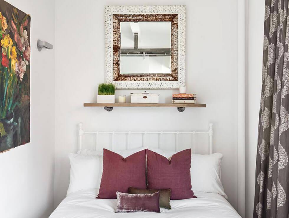 A small bedroom with white walls and a mirror to maximise light.
