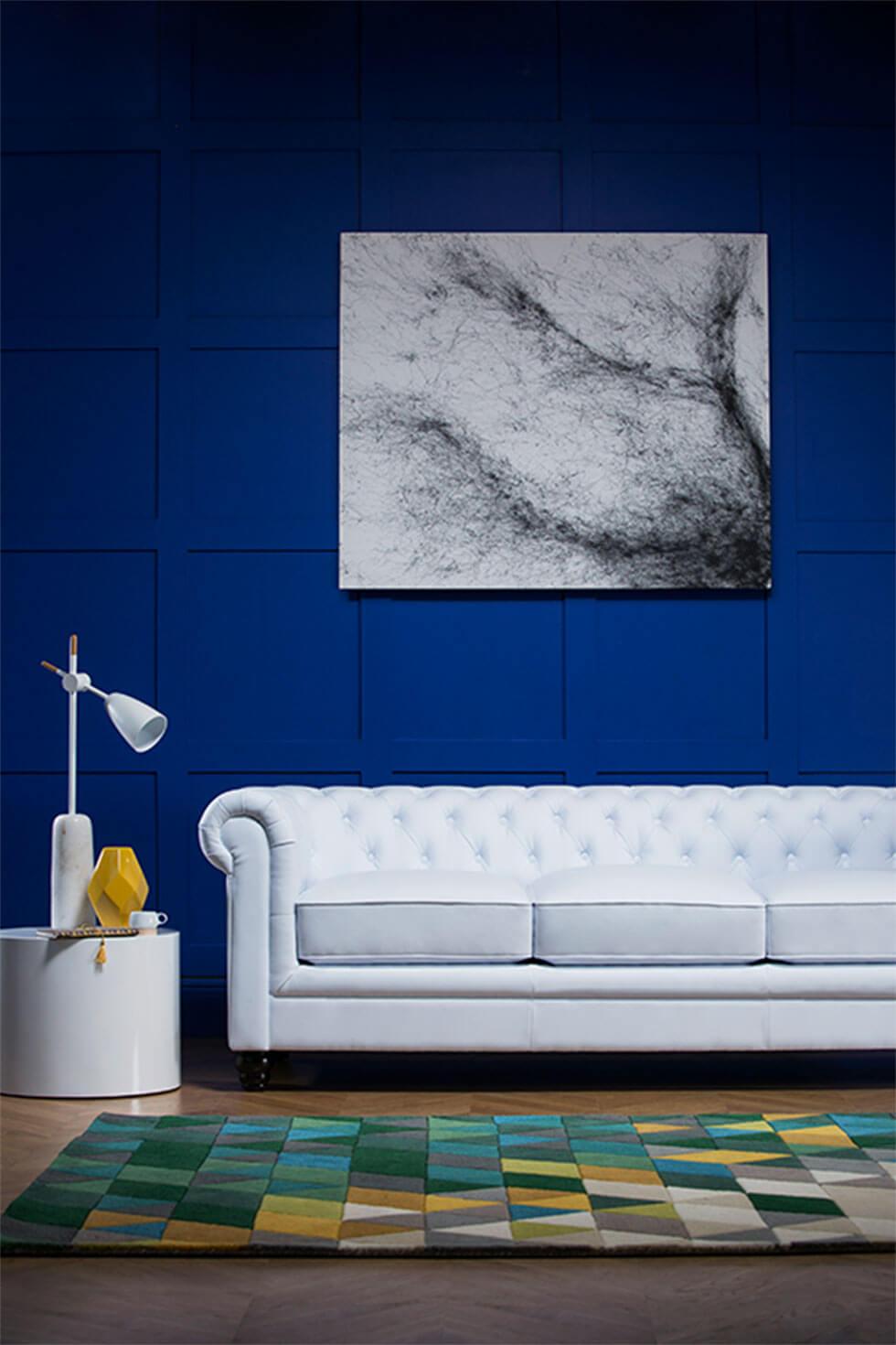 A white leather Chesterfield sofa in a living room with bold blue walls.