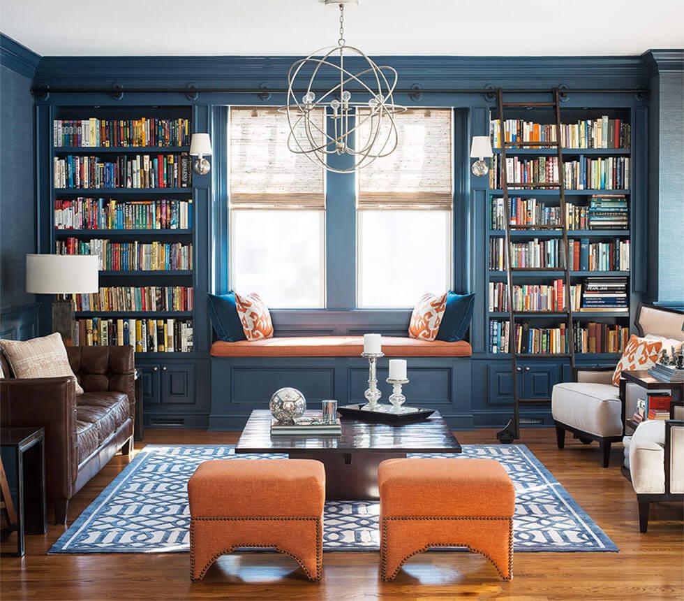 A blue living room with a home library and pops of orange.