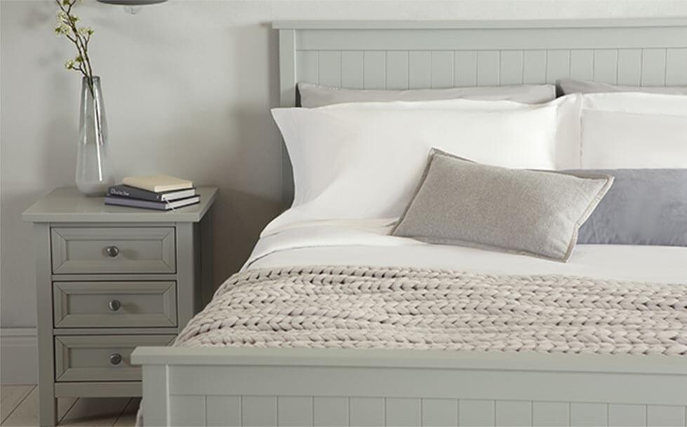 Grey bed layered with grey throw and pillows in a grey bedroom.