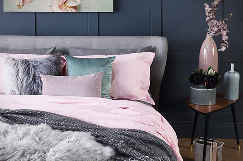 Grey upholstered bed, pink pillows in a dark grey bedroom.