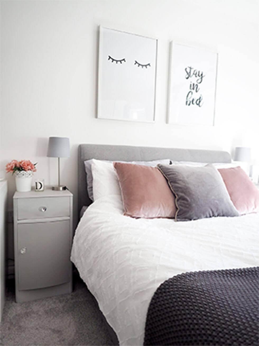 Light grey bed with dusty pink pillows in a light grey bedroom.