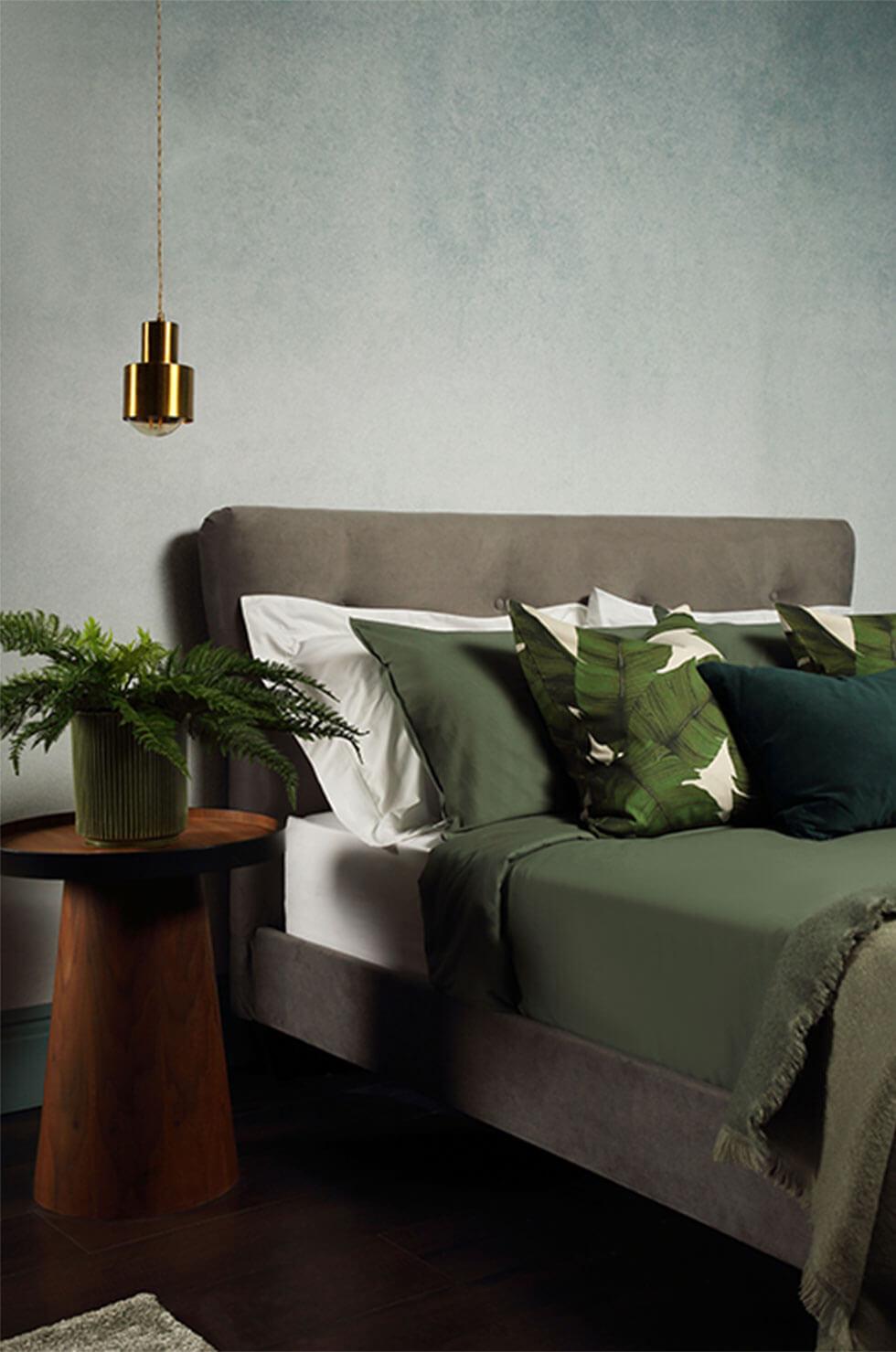 Grey velvet bed, green pillows in a grey bedroom.