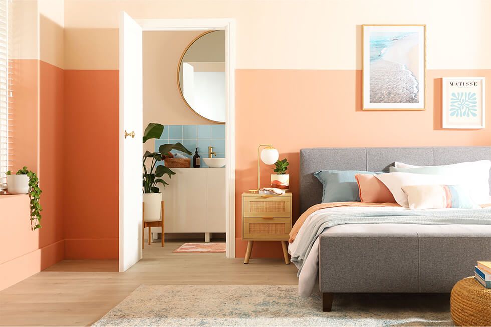 A summer bedroom with peach walls, grey fabric bed and beach wall art