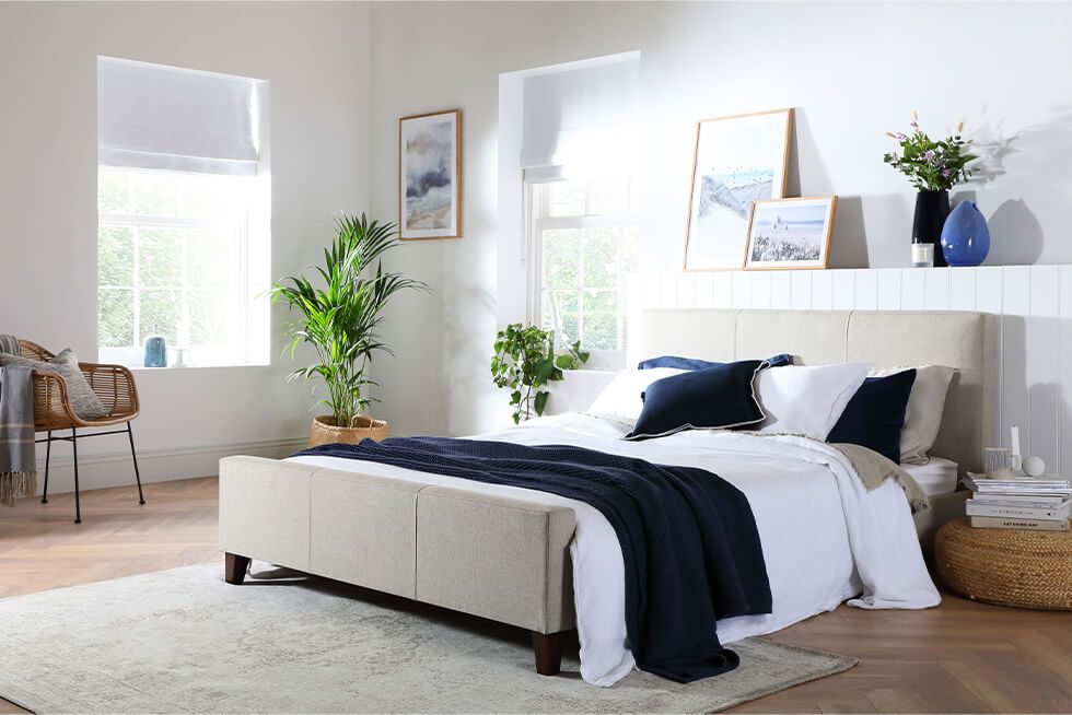 A coastal style summer bedroom with navy and white colours, and a beige fabric bed