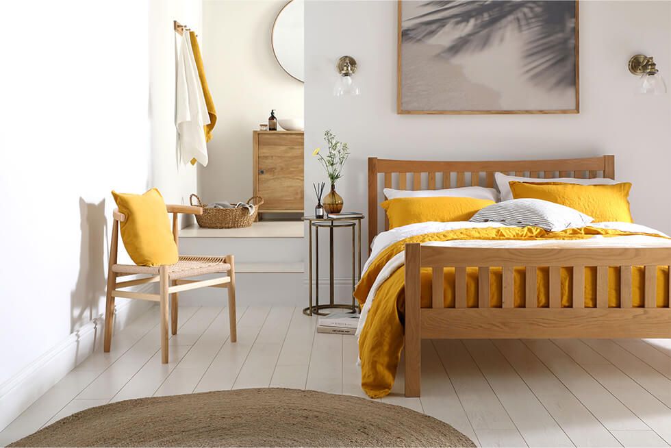 An oak bed with white and mustard yellow bedding, wooden frames and a woven rug