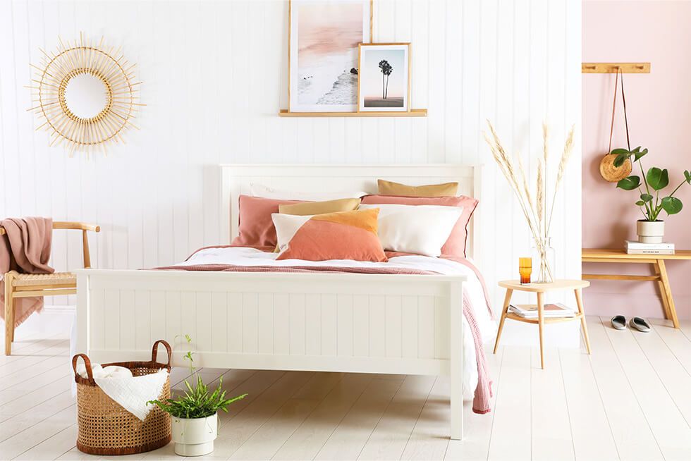 A summery white and pink bedroom with a white wooden bed and wall panels