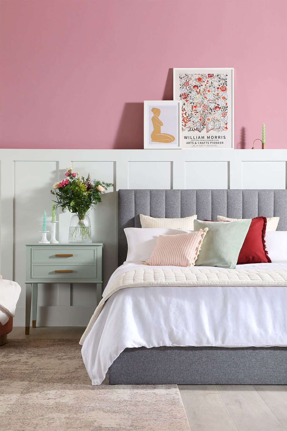 A contemporary summer bedroom with a pink half wall and white shaker style panels, grey fabric bed and pastel colours
