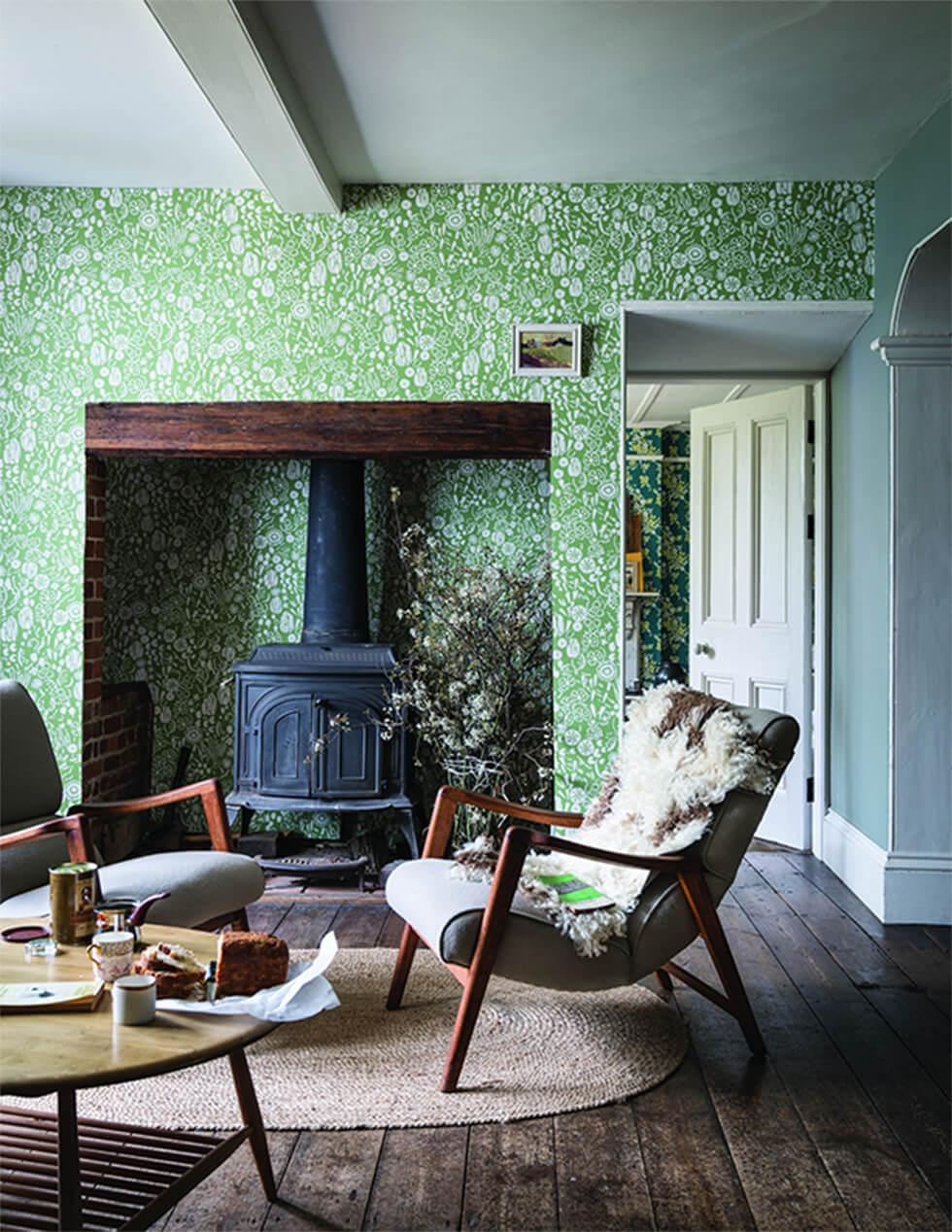 Green country living room with bright printed wallpaper, furnace, and low dark wood armchairs