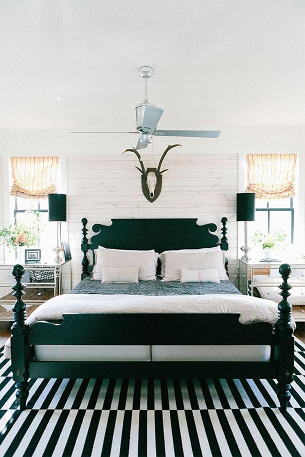 Black and white bedroom with black headboard and striped rug.