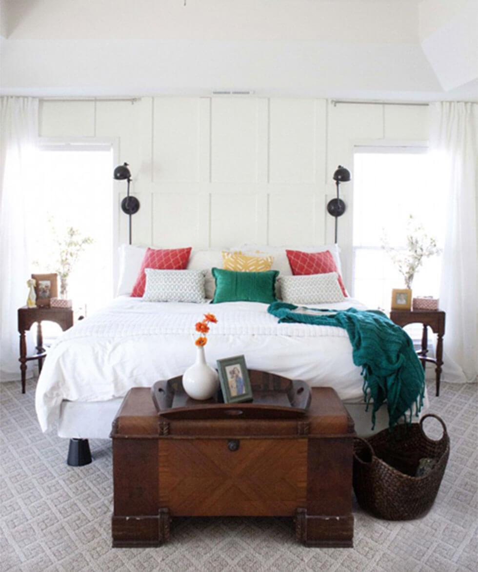 White bedroom with colourful throw pillows and wooden trunk.