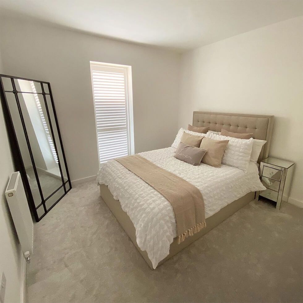 A spacious cream bedroom with a tufted bed and full-length mirror in the corner