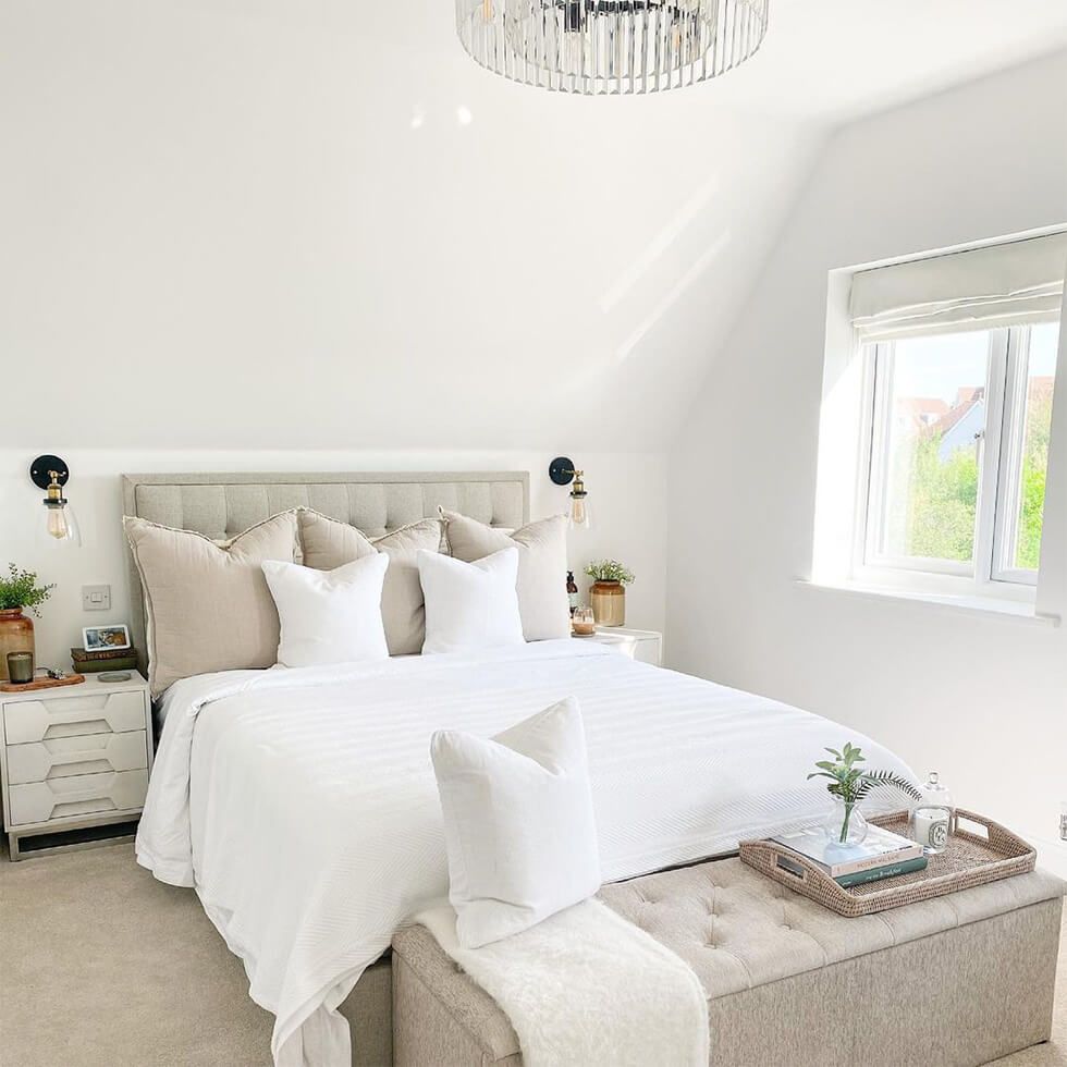 A bright bedroom with a cream tufted bed, white linens and a bench