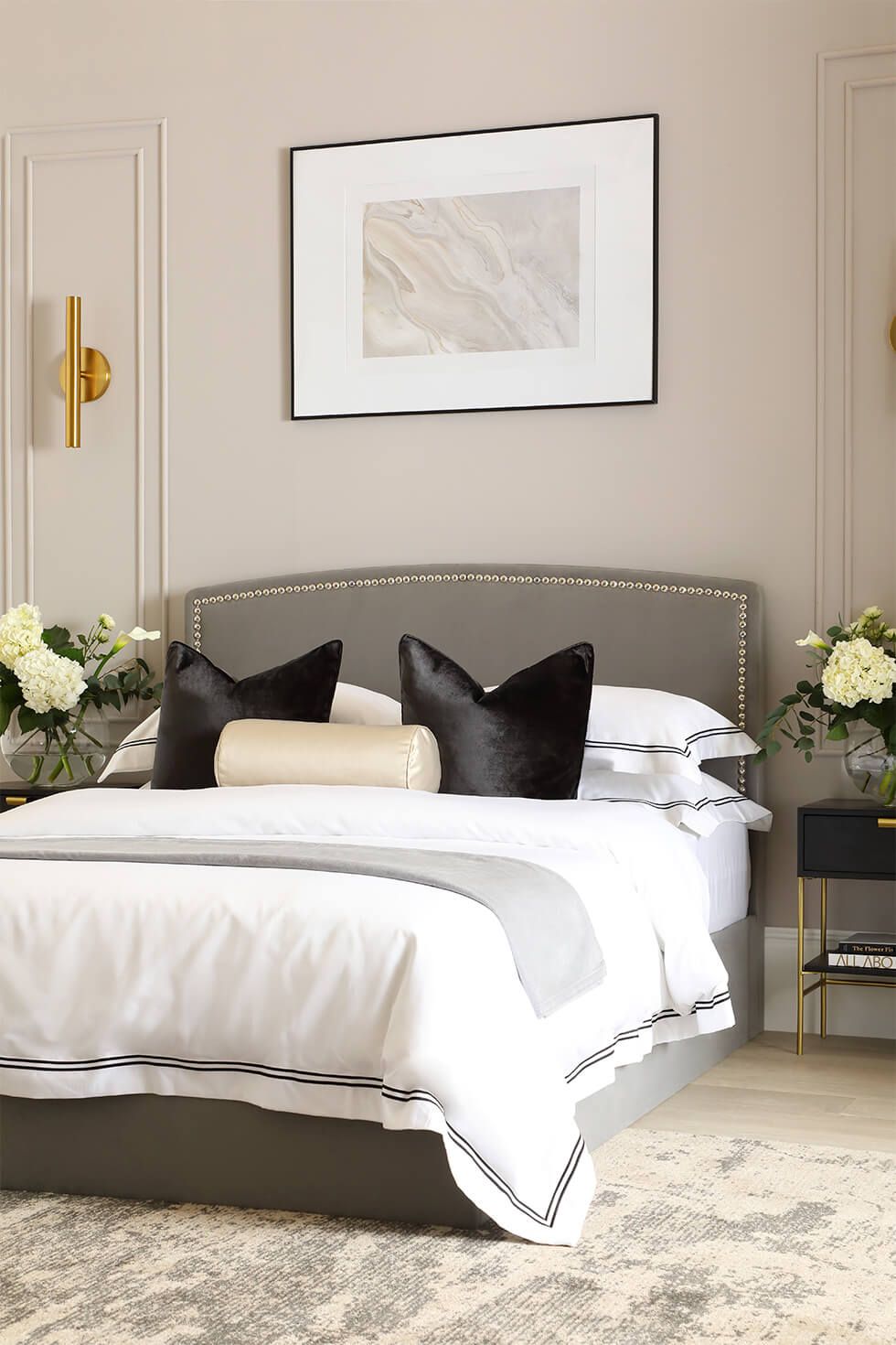 A luxurious bedroom with a velvet grey bed, black pillows and wall panelling
