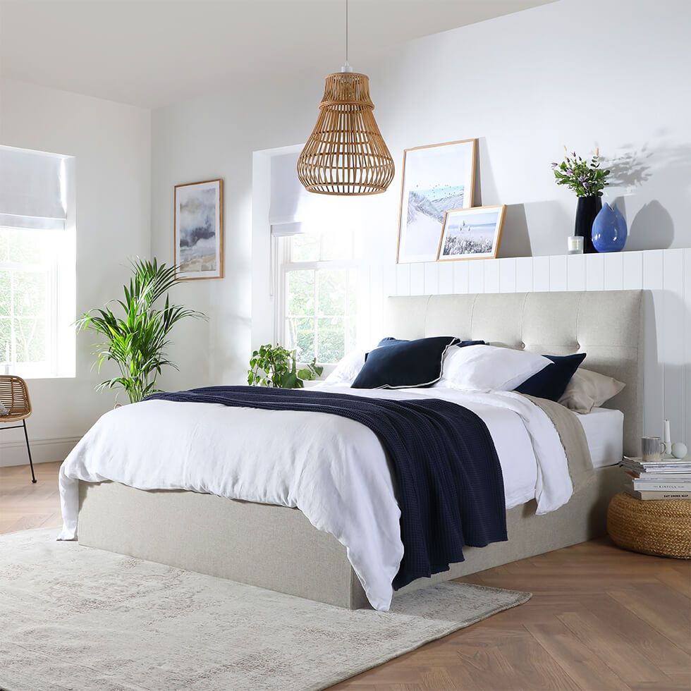 A coastal-inspired bedroom with a cream bed, scenic wall art and a rattan pendant light