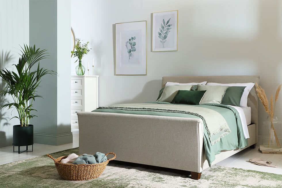 A calming bedroom styled with a cream bed, pastel green linens and fresh plants