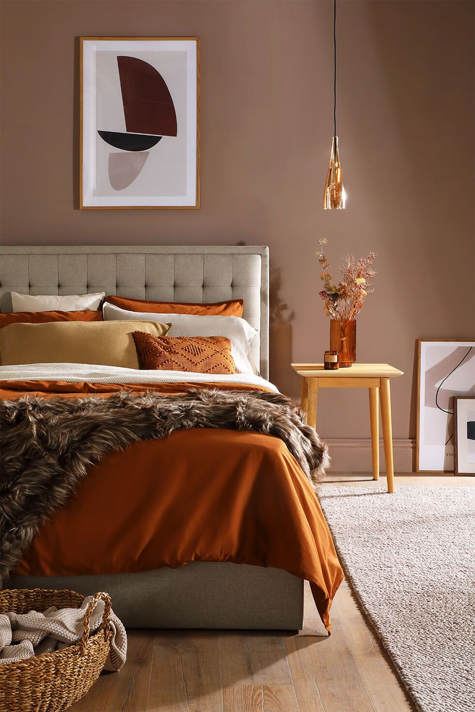 A warm bedroom styled with a tufted bed, layers of cosy linens and an abstract wall art