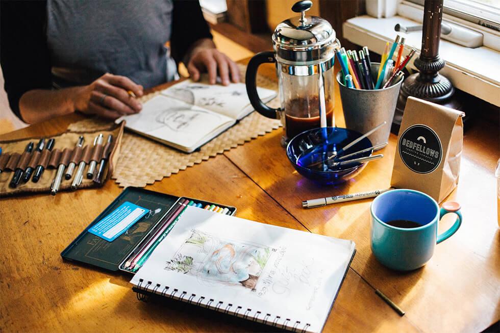 Person drawing in a sketchbook with pens and other materials.