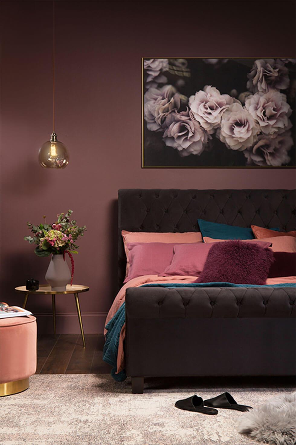 Black velvet bed with pink cushions and stool, with dark purple walls