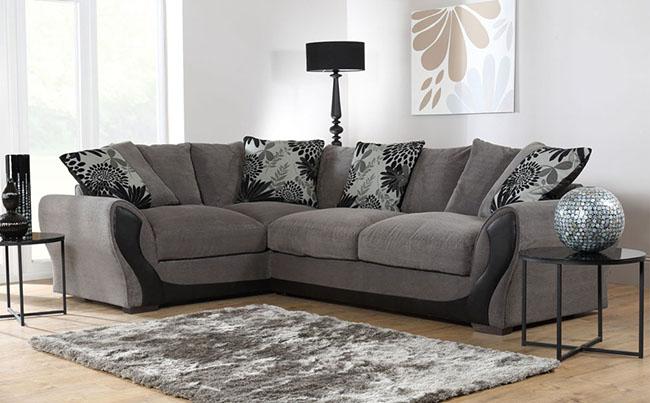 Grey corner sofa with a light grey rug against a brightly lit interior. 