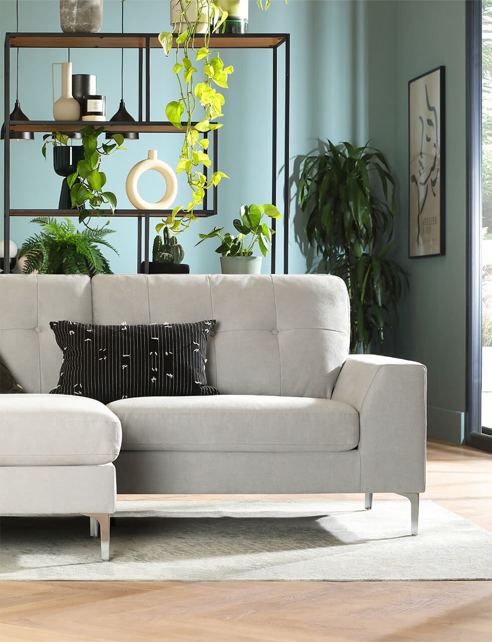 A stylish light grey sofa in an open plan living room with a tall shelving unit as a room divider