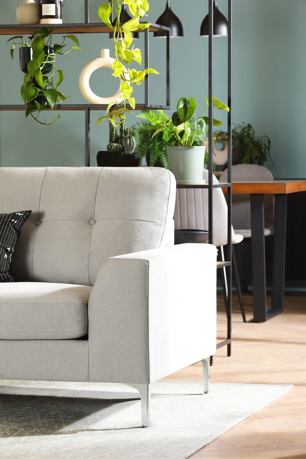 A shelving unit as a room divider between a stylish light grey sofa and industrial style dining set