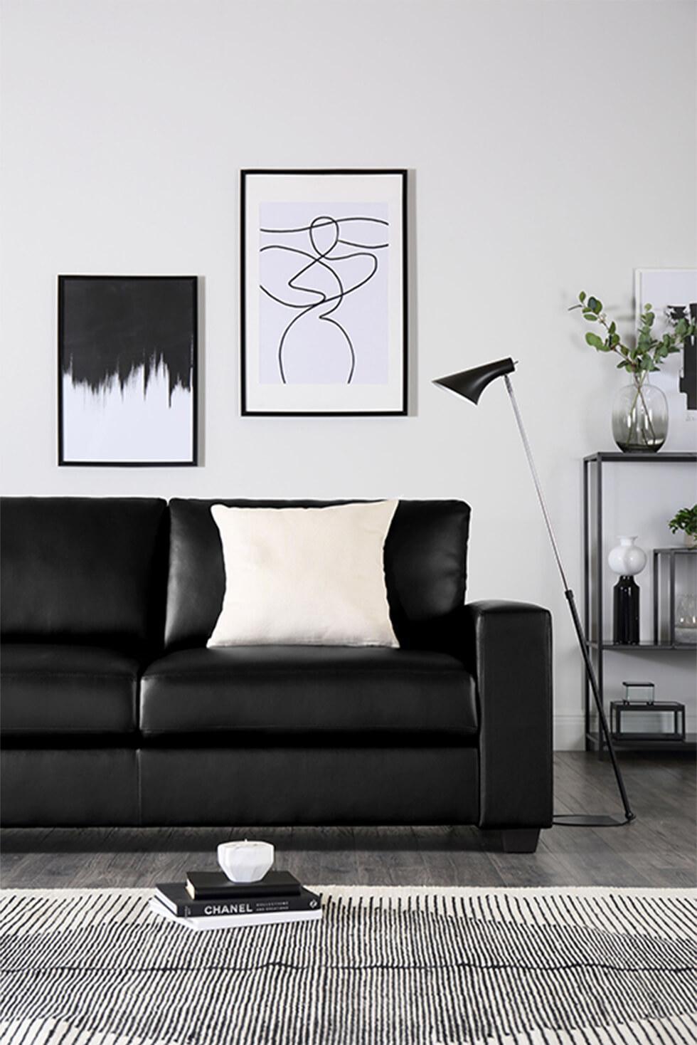 Clean monochrome living room with black leather sofa, framed art, striped rug and white cushion
