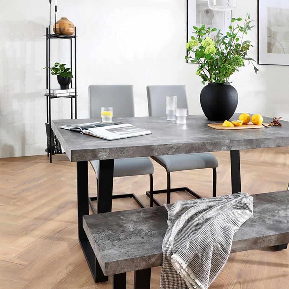 Industrial dining room with concrete dining table and bench and grey leather chairs with a vase of flowers