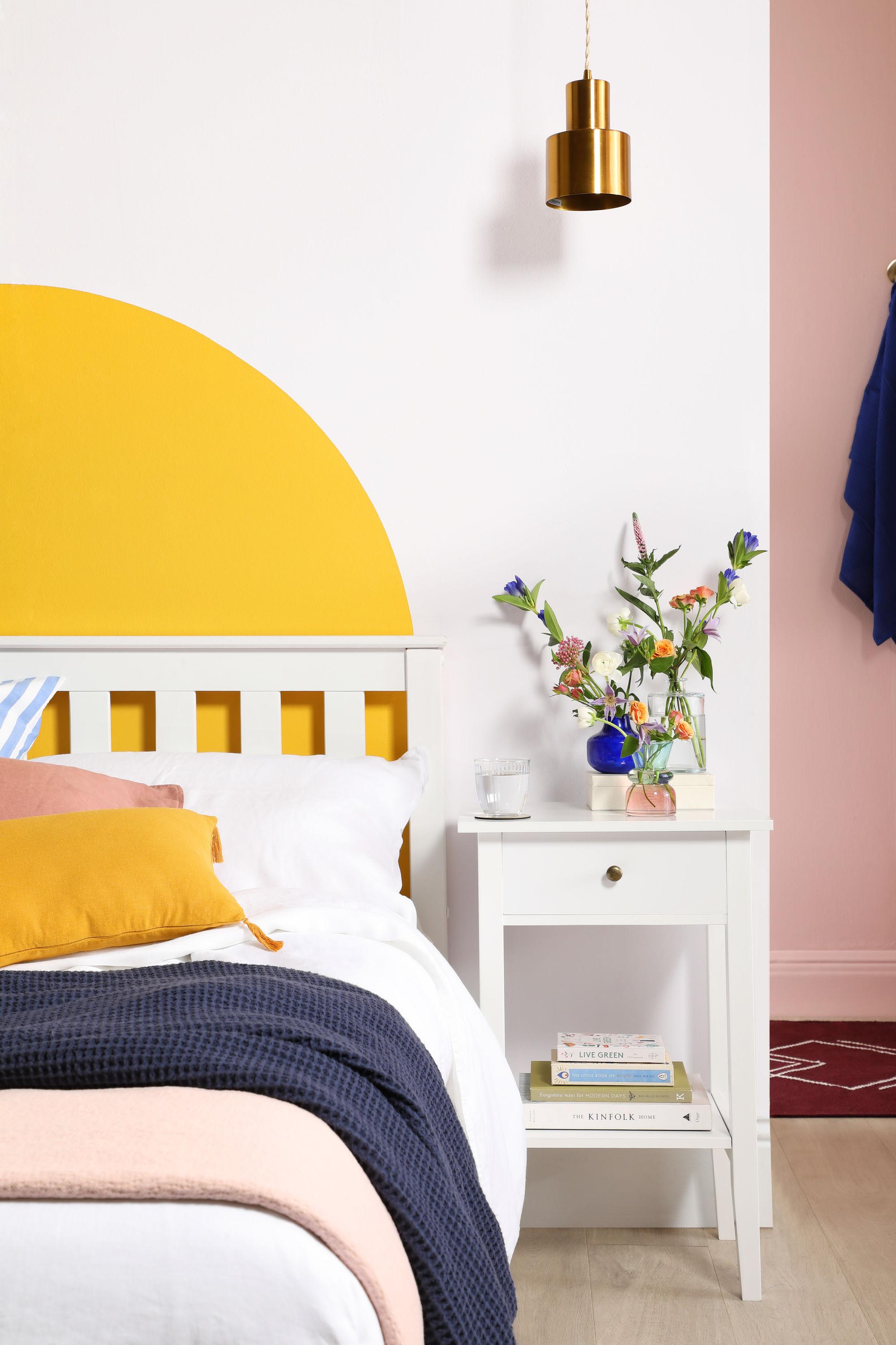 Pink and yellow bedroom with DIY painted headboard, striped, pink and mustard cushions and a white bed